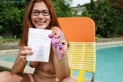 Girl in glasses sits open legged by the pool.